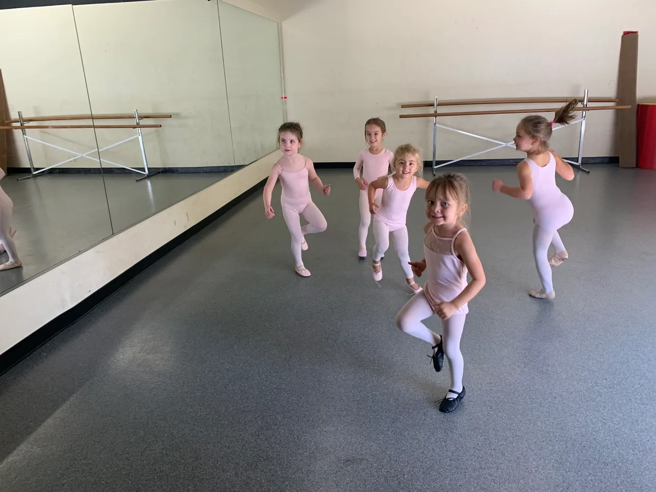 A group of young children in white outfits practicing ballet.