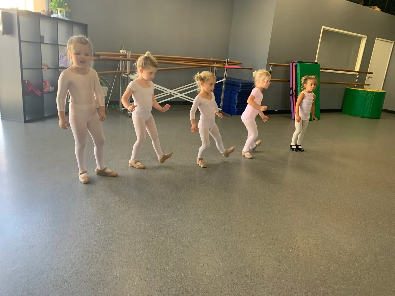 A group of young children in white leotards are standing.