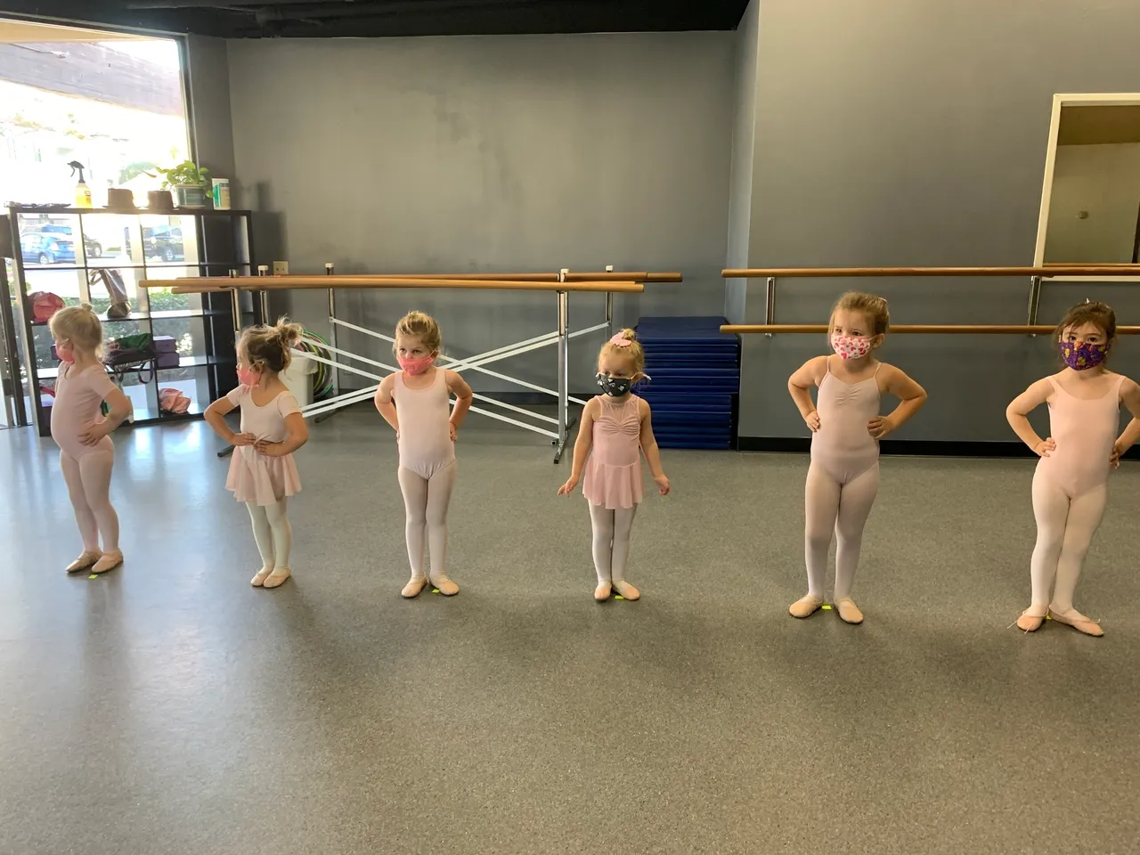 A group of young ballerinas standing in front of a row of ballet bars.
